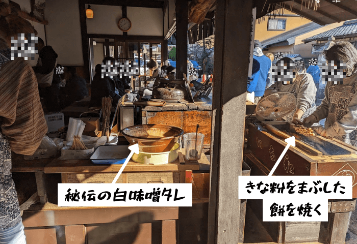 2024年1月2日の年始の実際の画像。
京都市の今宮神社参道であぶり餅を提供しているお店「一和」で、店員さんがあぶり餅を炭火であぶっている様子。秘伝の白味噌タレは大きな茶色の器に入っている。